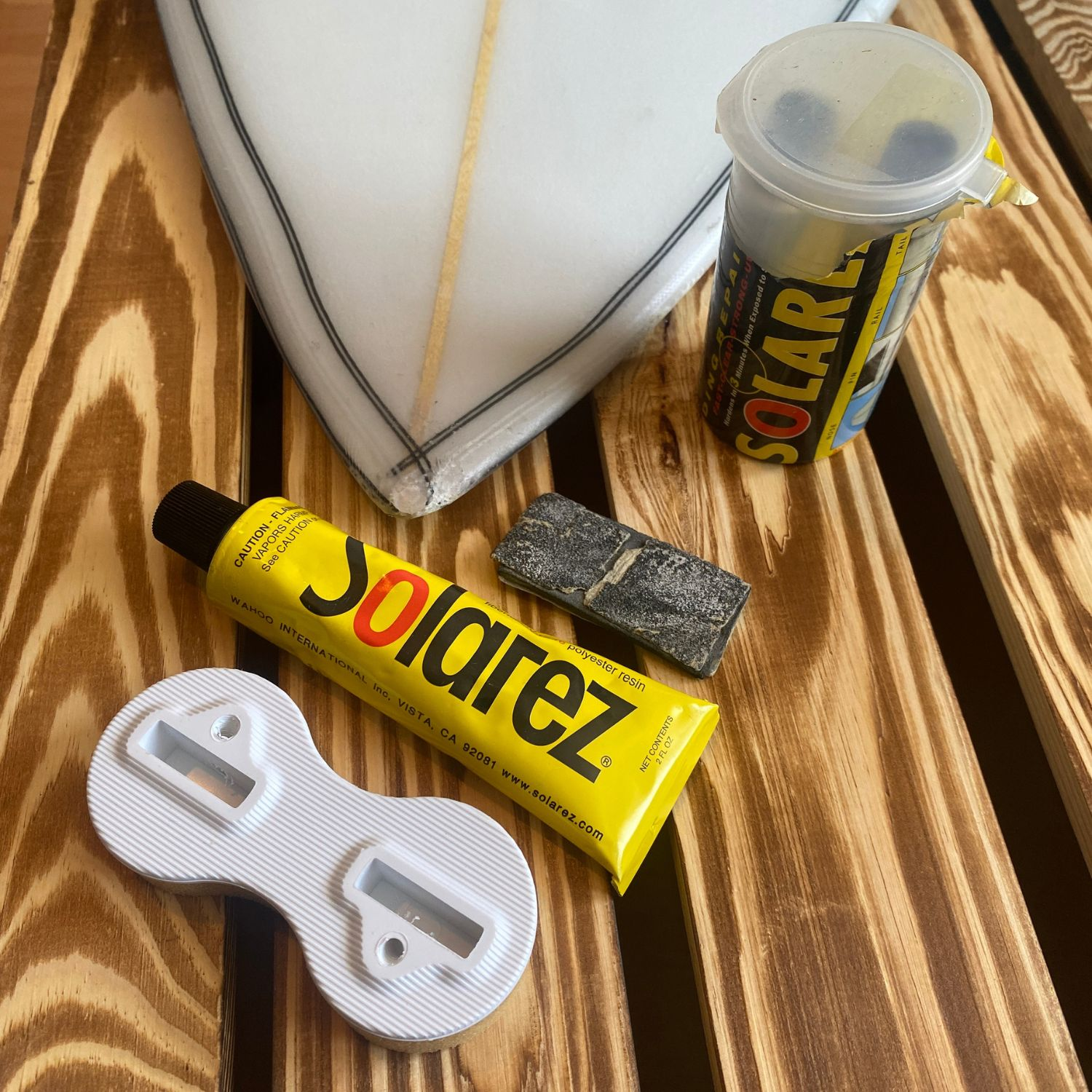 Solarez und Finnenkasten mit beschädigter Surfboard Nose auf Holz