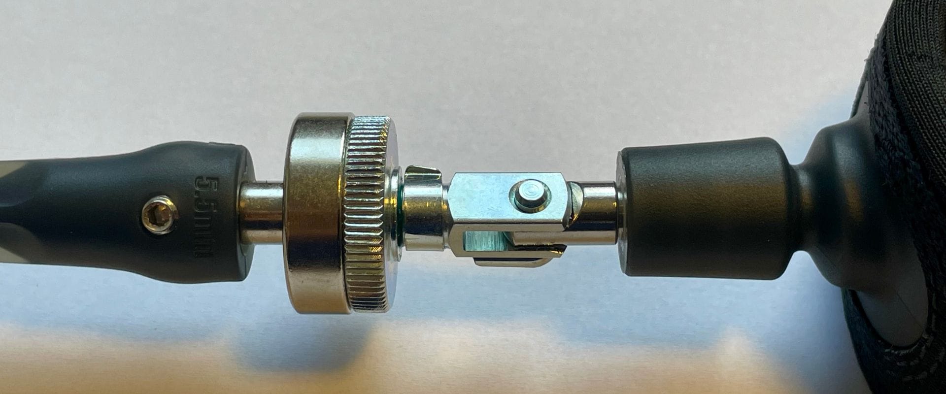 Nahaufnahme eines Gelenks aus Metall und Kunststoff, das zwei zylindrische Teile verbindet, möglicherweise ein verstellbarer Mechanismus oder ein Teil eines Geräts, mit sichtbaren Kerben und Verriegelungselementen.