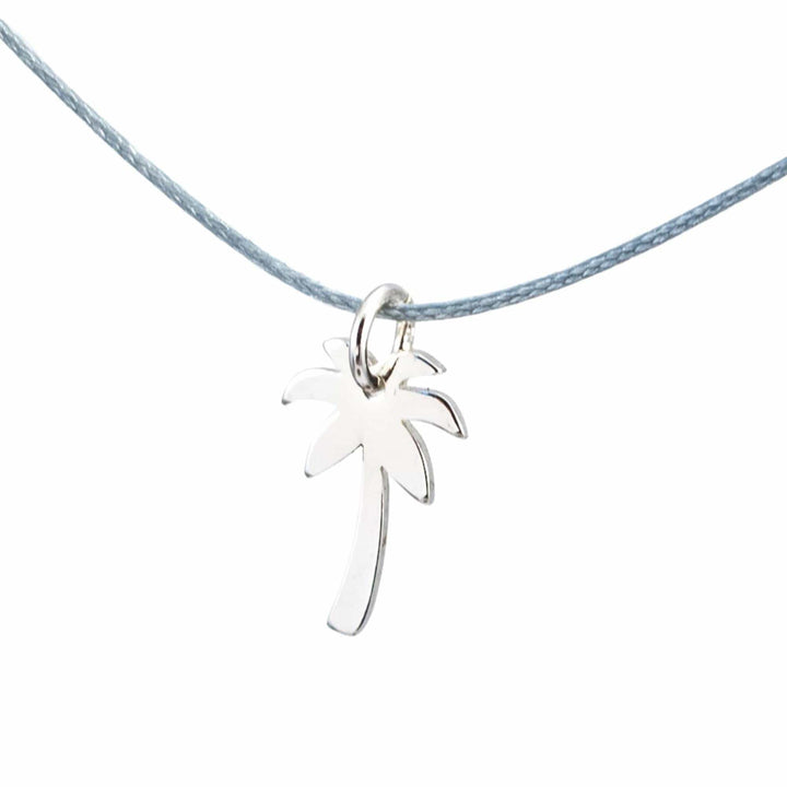 Der Silver+Surf Silber Schmuck Palme Anhänger aus 925 Sterling Silber hängt an einer dünnen, hellblauen Kordel - handgemachter Schmuck von Silver+Surf für stilvolle Akzente.