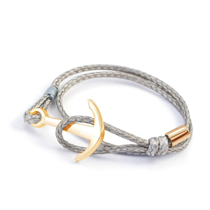Das Silver+Surf Silber Schmuck Boot Anker vergoldet verfügt über ein geflochtenes graues Kordelarmband mit einem vergoldeten ankerförmigen Verschluss und einem goldenen zylindrischen Akzent in der Nähe des Knotens.