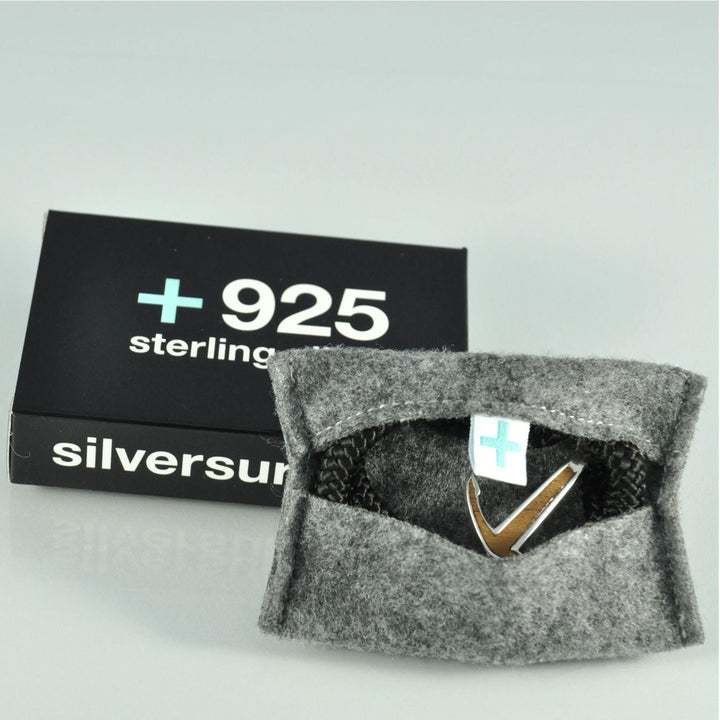Eine Schachtel mit der Aufschrift Silver+Surf steht neben einem geöffneten grauen Filzbeutel, in dem sich ein Silver+Surf Silber Schmuck Boot Anker Wood Armband befindet - silberner Schmuck, der sich perfekt mit Ihrem Lieblingslook kombinieren lässt.