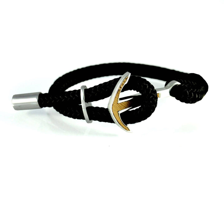 Das Silver+Surf Silber Schmuck Boot Anker Wood Armband verfügt über ein schwarzes, geflochtenes Seil, einen silbernen, ankerförmigen Verschluss, einen silbernen Ankeranhänger und eine silberne, zylindrische Endkappe, die alle vor einem weißen Hintergrund präsentiert werden.