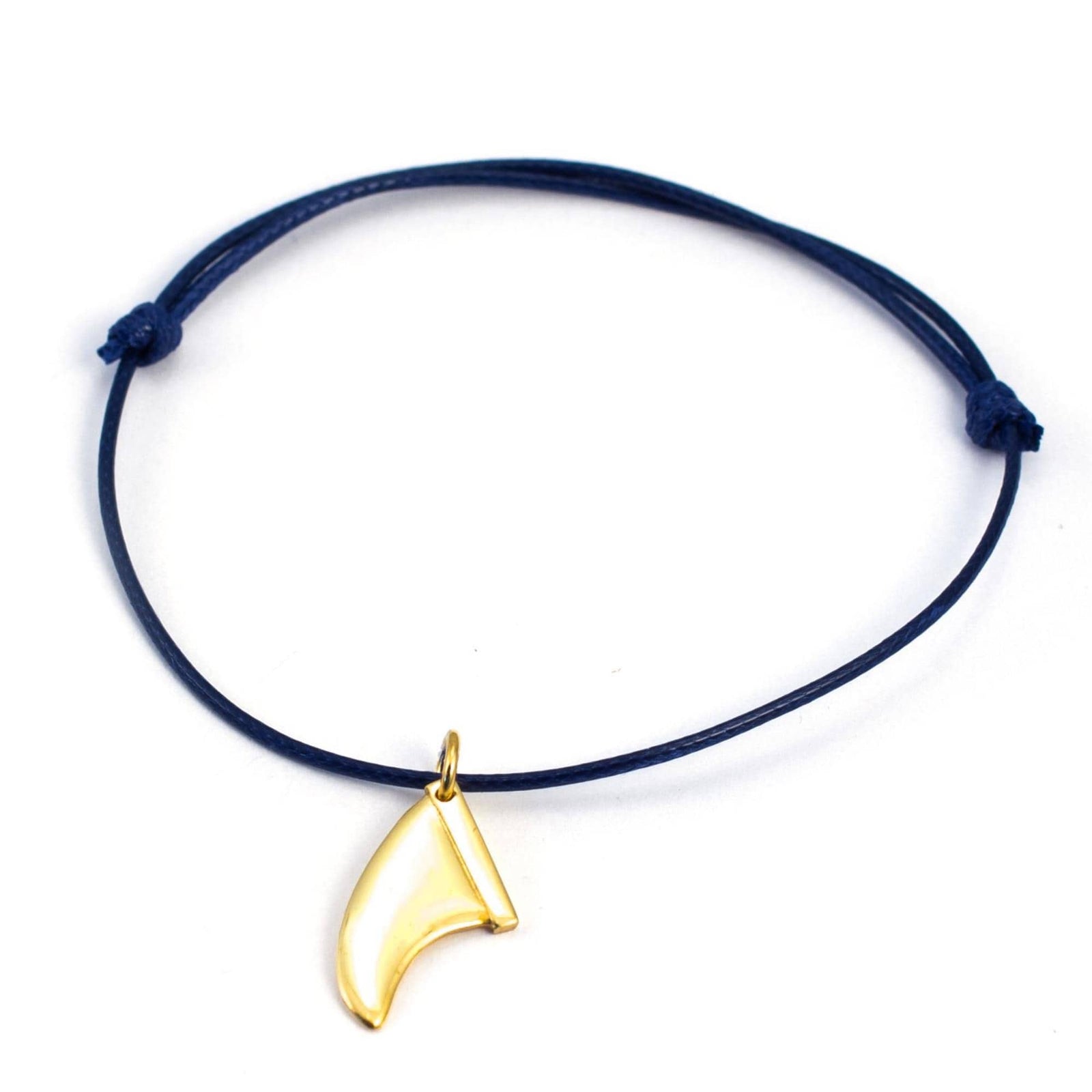Ein marineblaues Kordelarmband mit einem goldfarbenen Surfboard-Flossen-Charm von Silver+Surf, inspiriert von dem Golddesign der Silber Schmuck Surfboard Finne, auf weißem Hintergrund.
