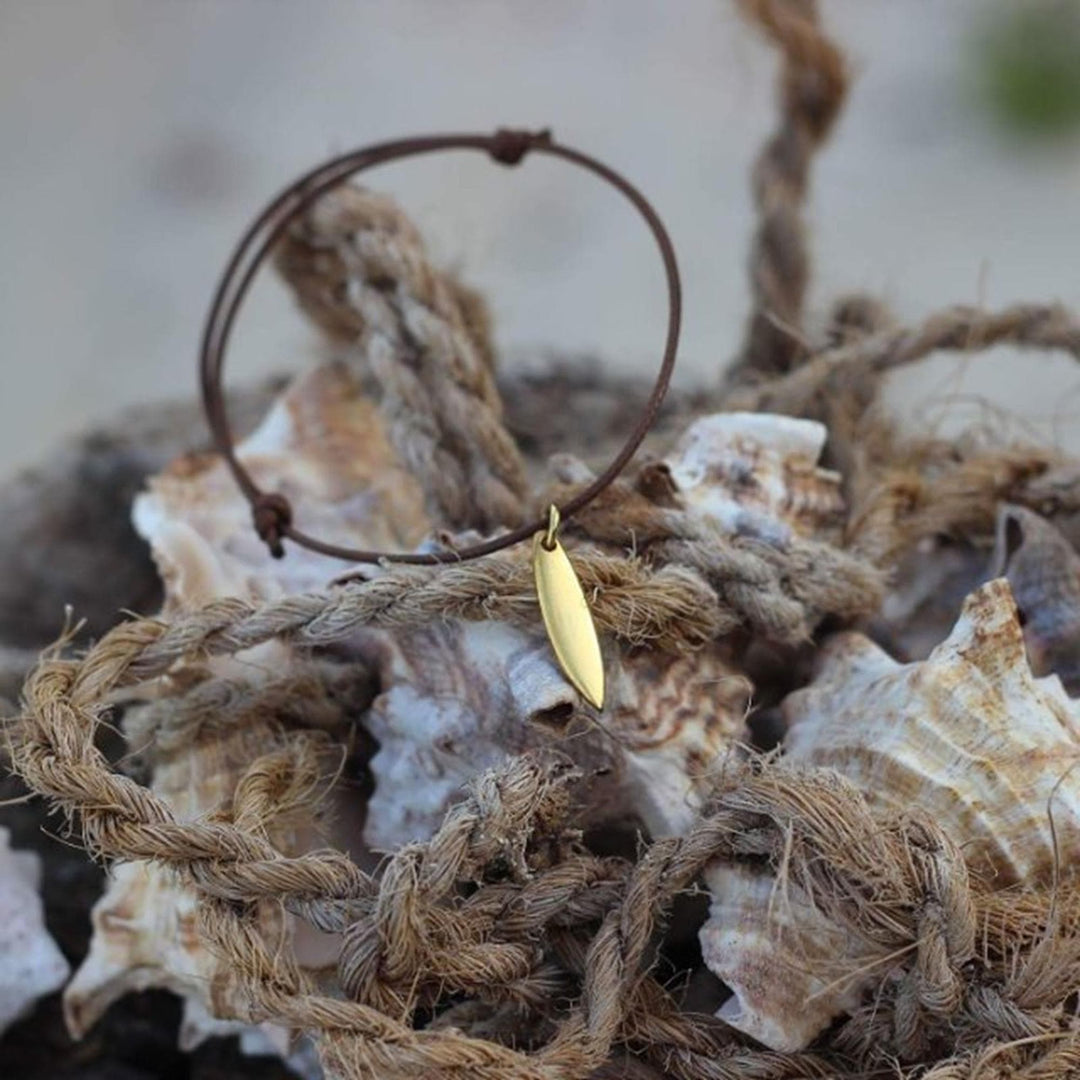 Das Goldarmband Silver+Surf Silber Schmuck Surfboard ist auf großen Muscheln und einem aufgerollten Seil abgebildet, mit einem sanft verschwommenen Hintergrund.