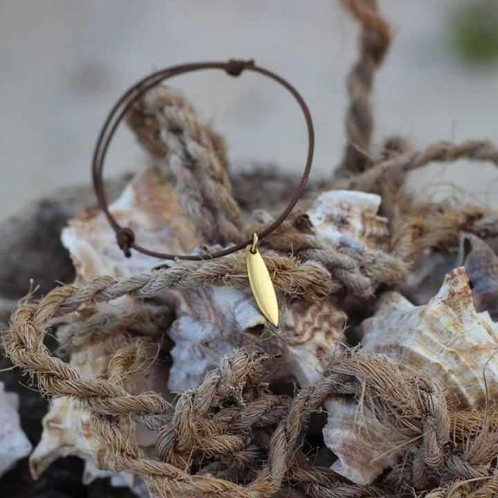 Das Goldarmband Silver+Surf Silber Schmuck Surfboard ist auf großen Muscheln und einem aufgerollten Seil abgebildet, mit einem sanft verschwommenen Hintergrund.