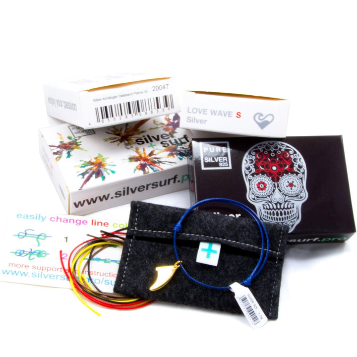 Die Silver+Surf-Schmuckverpackung besteht aus einem schwarzen Filzbeutel, einem Polypropylen-Armband mit mehrfarbigen Kordeln und der Silver+Surf Silber Schmuck Windrose Himmelsrichtung auf einer weißen Fläche.
