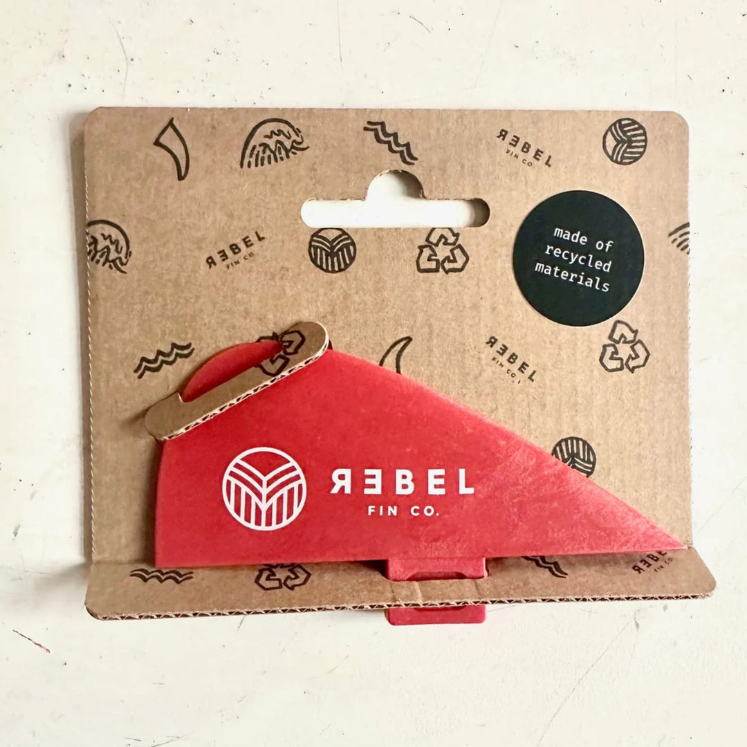 Die Surfari x Rebel Fin - Knubster Finne Glasfaser (rot) von Rebel Fin ist eine kleine rote Flosse aus recycelter Glasfaser, die auf einer Unterlage mit Wellen- und Recyclingsymbolen befestigt ist und einen Aufkleber "made of recycled materials" trägt.
