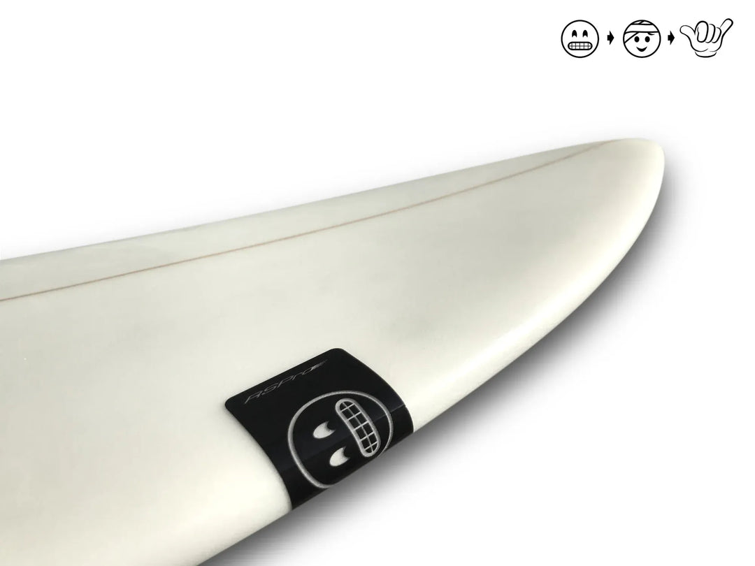 Nahaufnahme der Vorderseite eines weißen Surfboards mit einem kleinen schwarzen Aufkleber, der ein zahniges Lächeln zeigt. Drei Icons in der oberen rechten Ecke markieren RSPro Surfboard Ding Patches (6 Stück) und selbstklebende Patch-Optionen von RSPro.