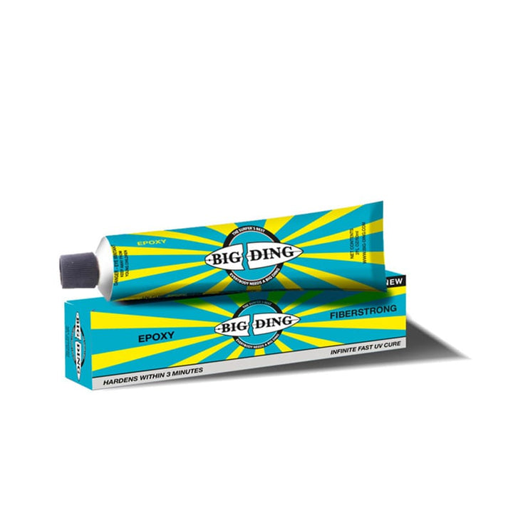 Eine Tube Big Ding Epoxy Fiberstrong UV Cure ruht auf der passenden blauen Schachtel mit gelben Strahlen und dem Big Ding Logo. Der Text hebt die schnelle UV-Härtung für die Reparatur von Surfboards hervor, die in nur 3 Minuten aushärtet.