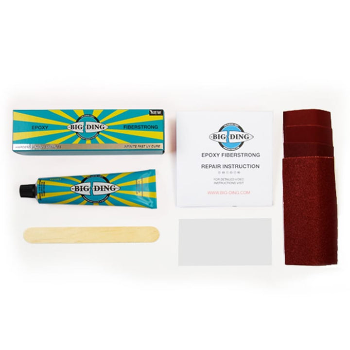 Das Big Ding Epoxy Fiberstrong UV Cure Reparaturset von Big Ding enthält UV-härtendes Epoxidharz, einen Holzstab, eine Plastikkarte, Schleifpapierblätter und eine Anleitung - alles übersichtlich auf einer weißen Fläche angeordnet.
