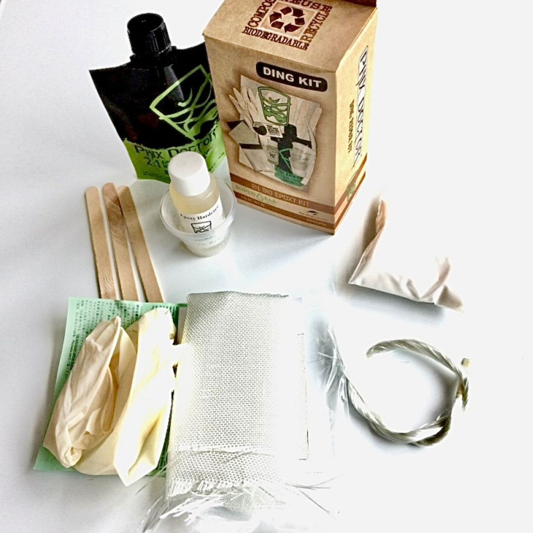 Das PHIX DOCTOR Bio-Epoxy Ding Repair Kit Small (3oz/90ml) wird auf einer weißen Fläche mit Handschuhen, Holzstäbchen, Schleifpapier, Harz, Glasfasertuch, Mischbeutel, Bio-Epoxidharz-Pulverpackung und einer "Ding Kit"-Box gezeigt.