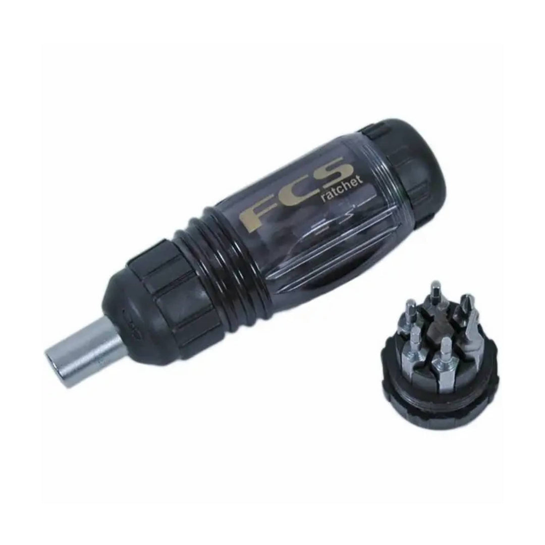 Das FCS Ratchet Tool (für Finnenschrauben) von FCS mit schwarzem und transparentem Griff wird neben einem runden Halter mit mehreren austauschbaren Bits gezeigt - ideal für die Einstellung der Finnenschlüssel auf dem Surfbrett.
