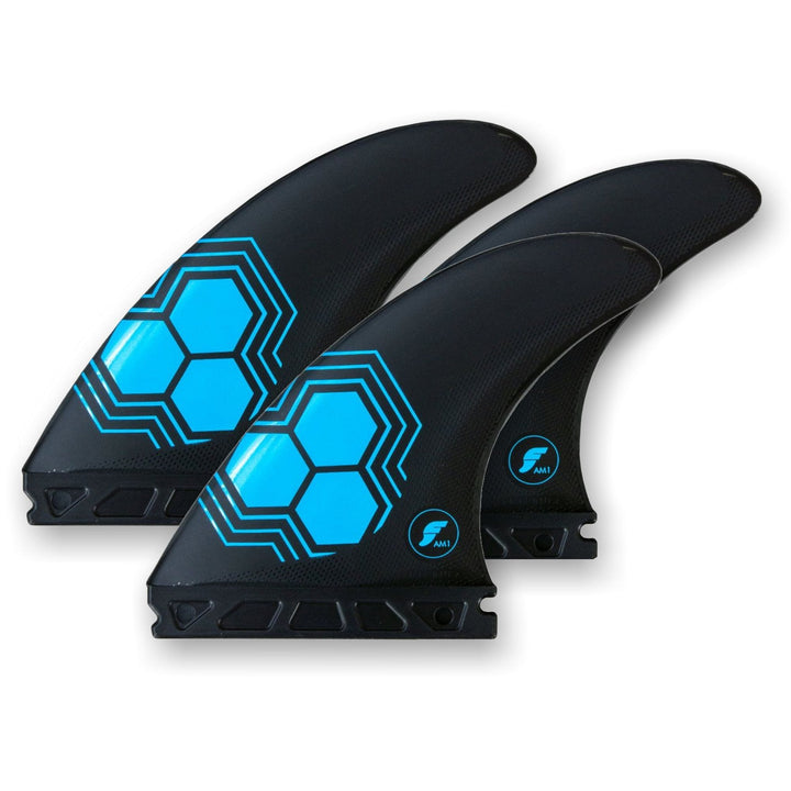 Drei schwarze FUTURES Thruster Finnen Set AM1 Al Merrick Alpha Surfboard Finnen von futures, mit blauen Sechseckmotiven und einem kleinen FM II Logo, sind nebeneinander auf weißem Hintergrund angeordnet. Ideal für Channel Islands Surfboards und Thruster Setups.