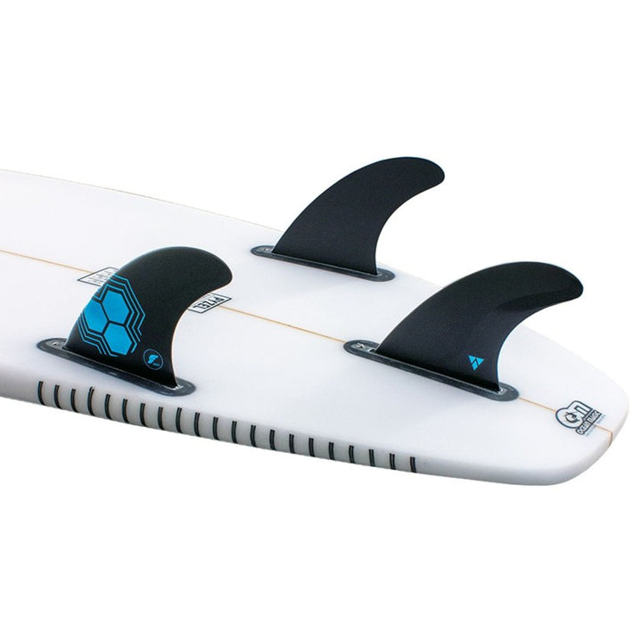 Nahaufnahme eines Channel Islands Surfboard Hecks mit dem futures AM1 Al Merrick Alpha Thruster Finnen Set in schwarz. Das weiße Board hat eine dünne orangefarbene Mittellinie und blau-schwarze Grafiken in der Nähe der Finnenkästen.