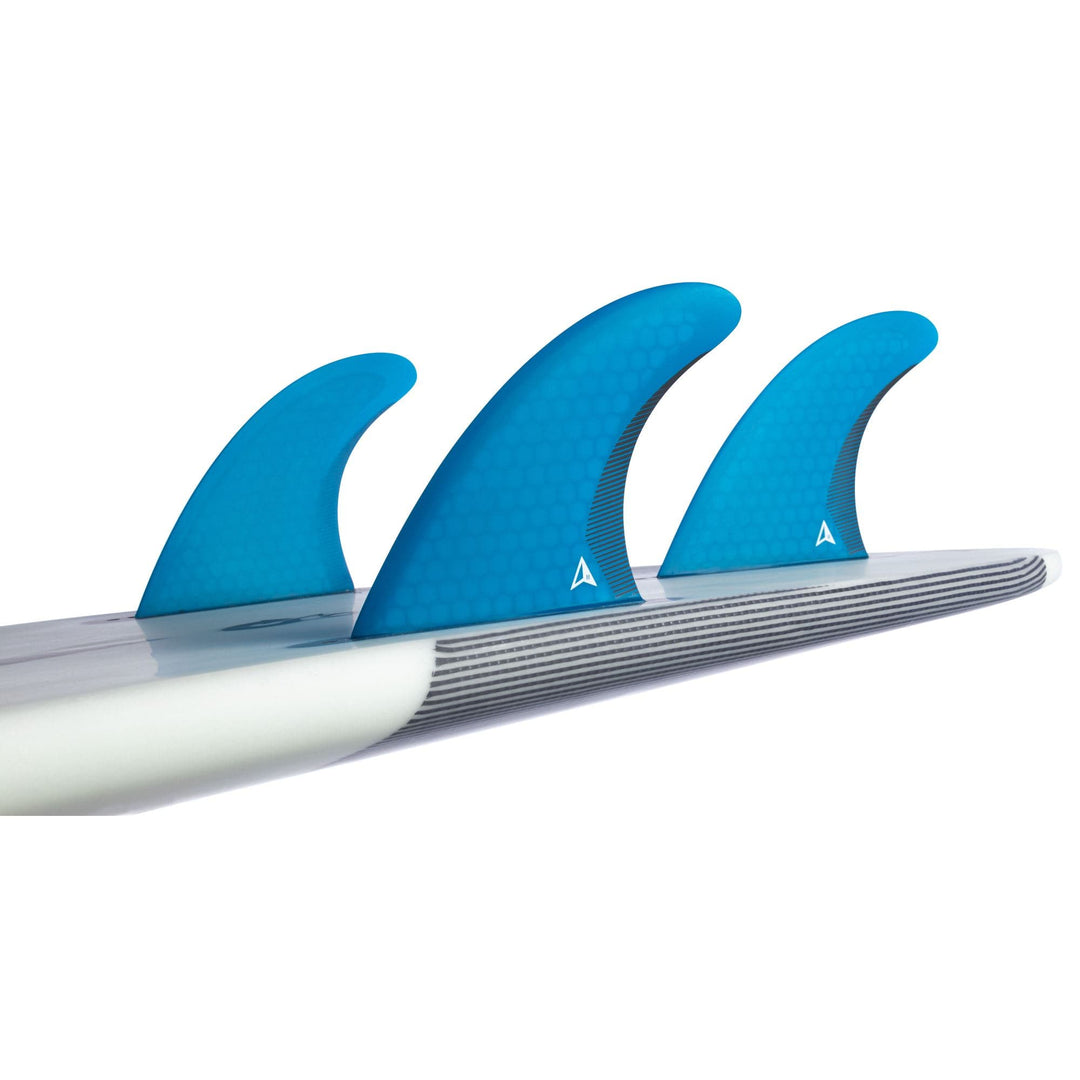 Eine Nahaufnahme des ROAM Thruster Fin Set Performer one tab von Roam - drei blaue Finnen mit Wabenmuster und kleinen dreieckigen Logos - montiert auf einem Performance Shortboard mit glatten weiß-grau gestreiften Kanten.