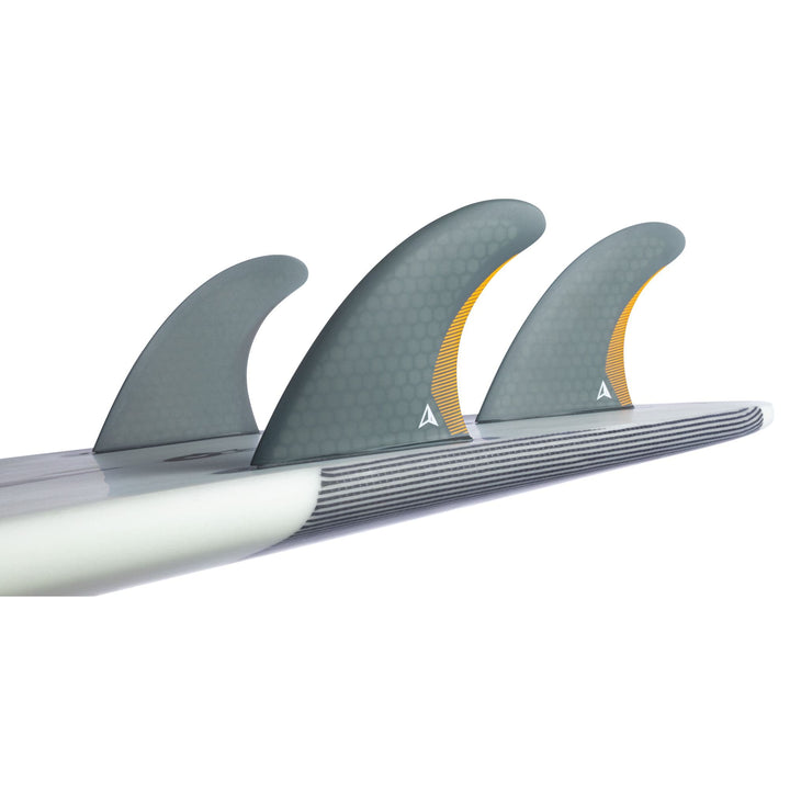 Nahaufnahme der Seitenansicht des ROAM Thruster Fin Set Performer two tab von Roam, die drei graue Wabenfinnen mit orangefarbenen Akzenten zeigt, die auf der Unterseite eines Surfbretts montiert sind, vor einem weißen Hintergrund. Ideal für Performance-Surfen.