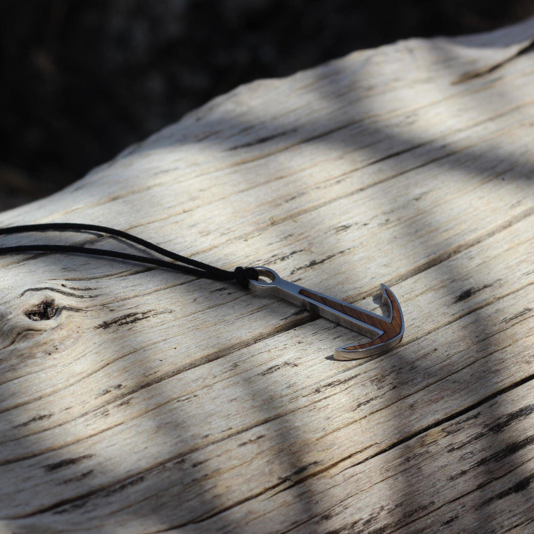 Das Silver+Surf Silber Schmuck BootAnker Wood Halsband von Silver+Surf mit silbernem Anker und Holzakzenten auf dunkler Kordel liegt auf verwittertem Holz.