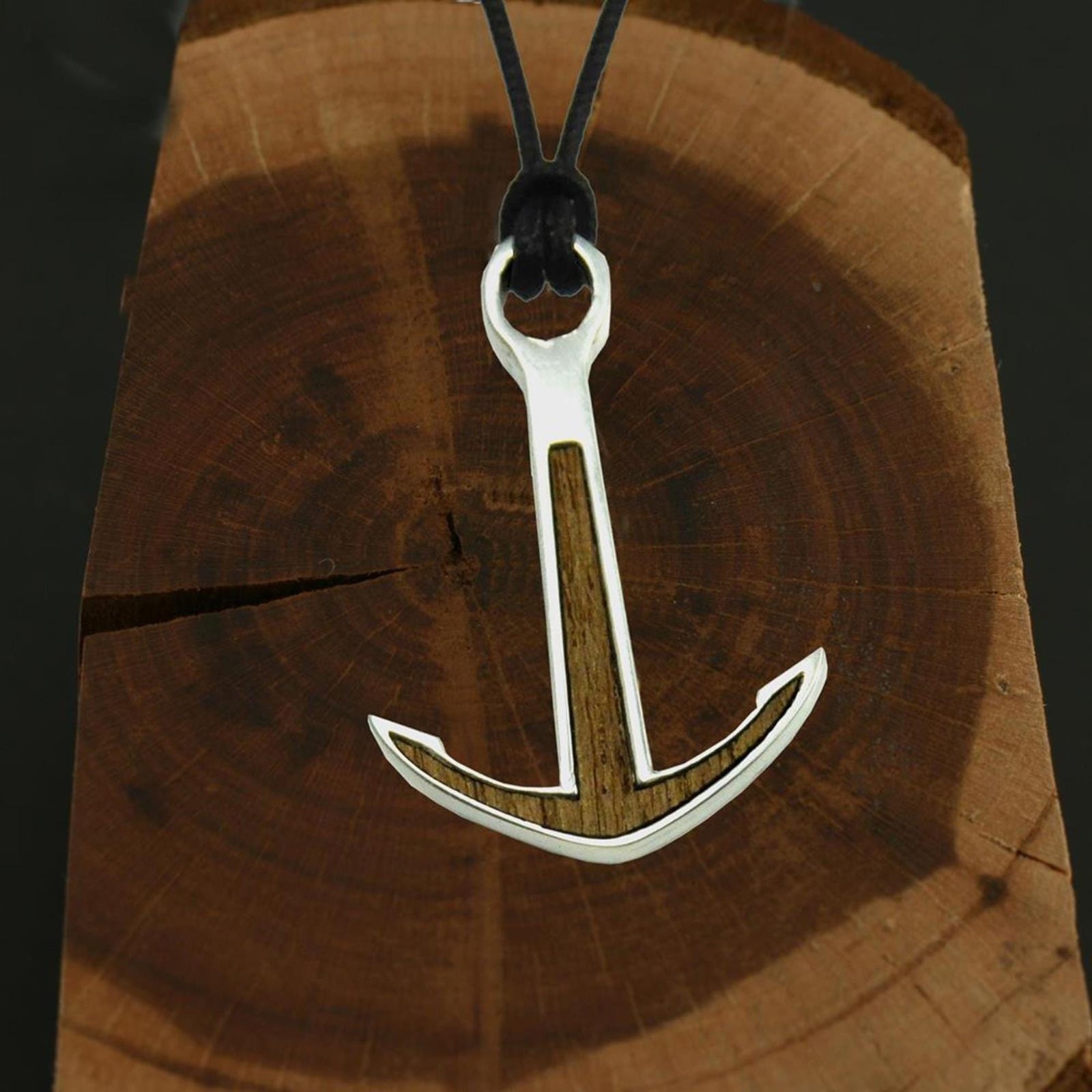 Das Silver+Surf Silber Schmuck BootAnker Wood Halsband - ein handgemachter 925 Sterling Silber Anhänger mit Holzintarsie am schwarzen Band - präsentiert sich auf einer Baumquerschnittscheibe.
