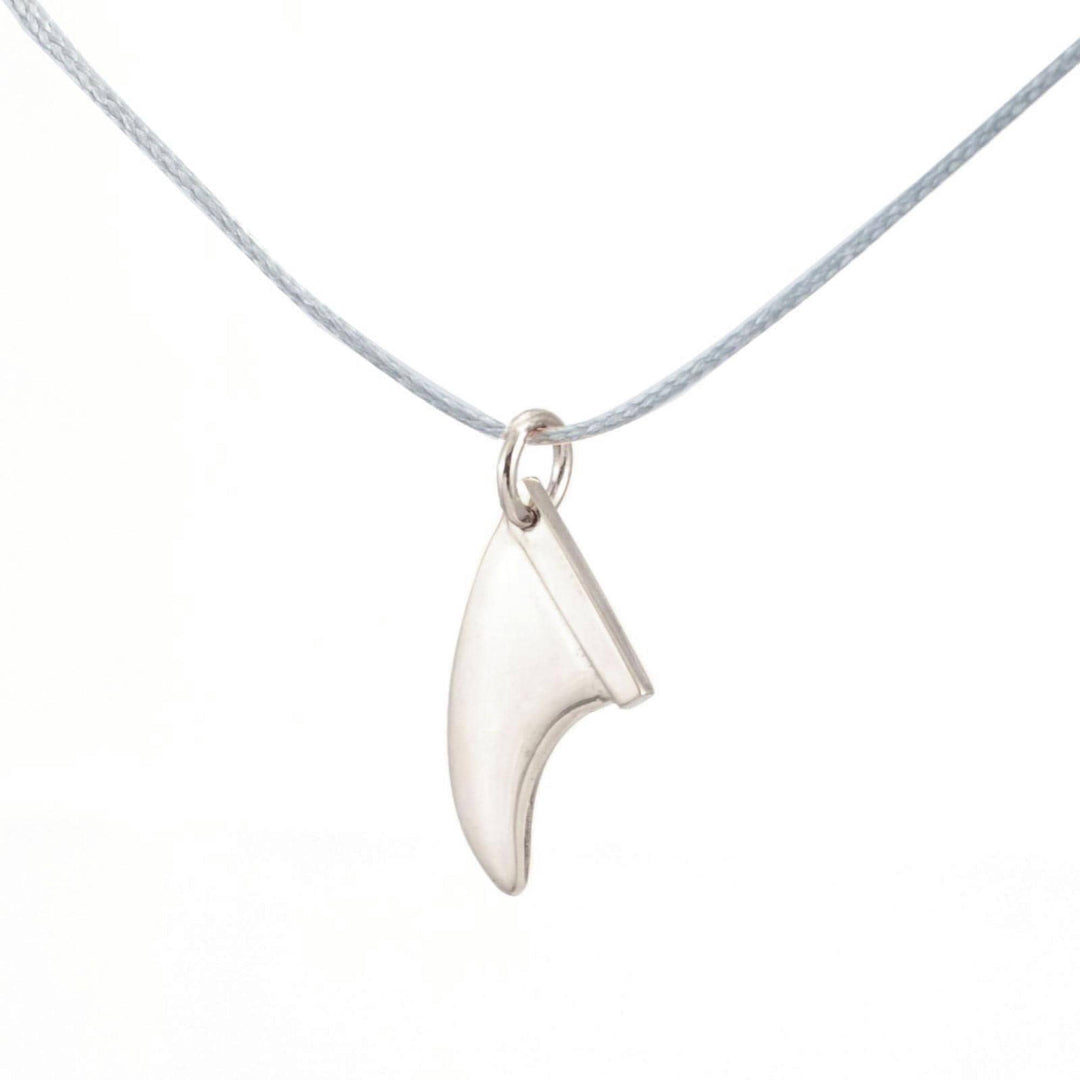 Die Silver+Surf Silber Schmuck Surfboard Finne, ein fangförmiger 925 Sterling Silber Anhänger, hängt an einer dünnen grauen Kordel vor einem weißen Hintergrund und repräsentiert eleganten handgefertigten Schmuck von Silver+Surf.