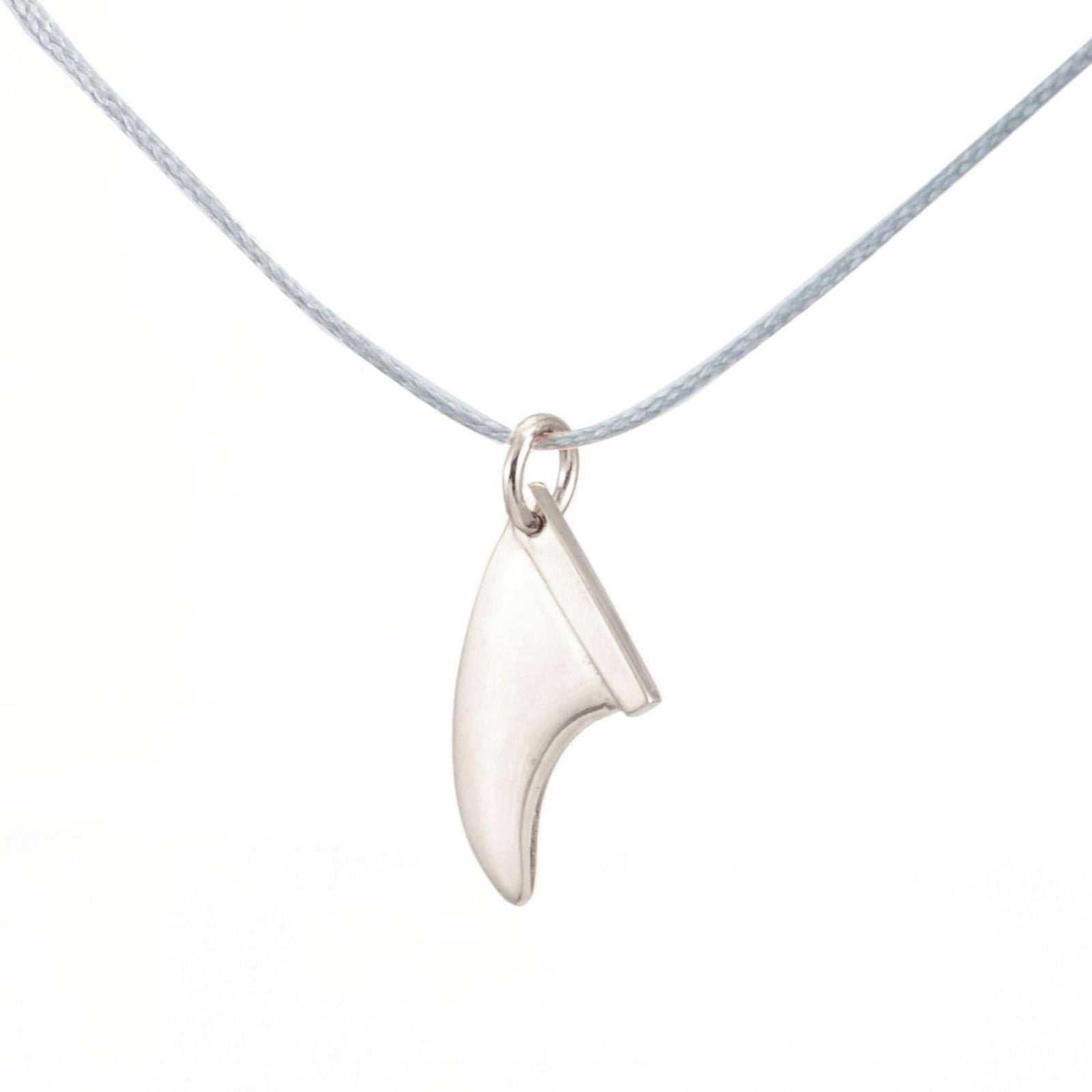 Die Silver+Surf Silber Schmuck Surfboard Finne, ein fangförmiger 925 Sterling Silber Anhänger, hängt an einer dünnen grauen Kordel vor einem weißen Hintergrund und repräsentiert eleganten handgefertigten Schmuck von Silver+Surf.