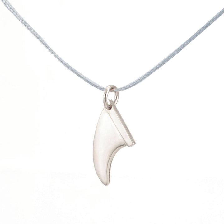 Die Silver+Surf Silber Schmuck Surfboard Finne, ein fangförmiger 925 Sterling Silber Anhänger, hängt an einer dünnen grauen Kordel vor einem weißen Hintergrund und repräsentiert eleganten handgefertigten Schmuck von Silver+Surf.