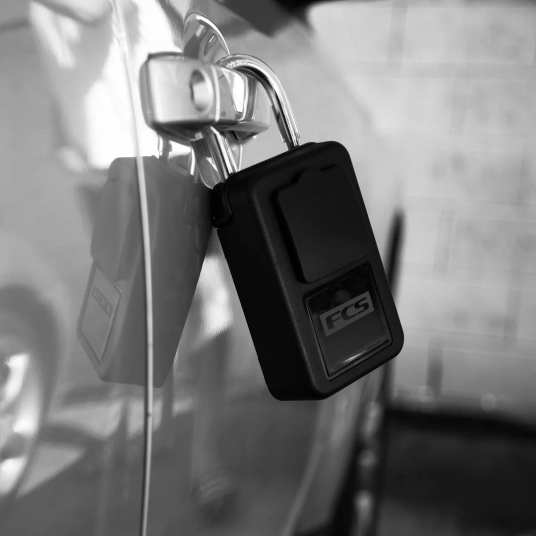 Eine schwarz-weiße Nahaufnahme zeigt das FCS - Keylock Groß/Large von FCS, das an einem Autotürgriff befestigt ist und demonstriert, wie Sie Ihren Autoschlüssel sicher aufbewahren können.