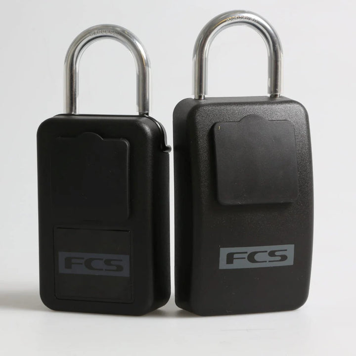 Zwei schwarze rechteckige FCS - Keylock Groß/Large Schließfächer mit silbernen U-förmigen Bügeln stehen aufrecht nebeneinander, jeweils beschriftet mit "FCS" auf der Vorderseite und einem Deckel darüber - ideal zum Autoschlüssel sicher aufbewahren als Surfer Schlüsselsafe.