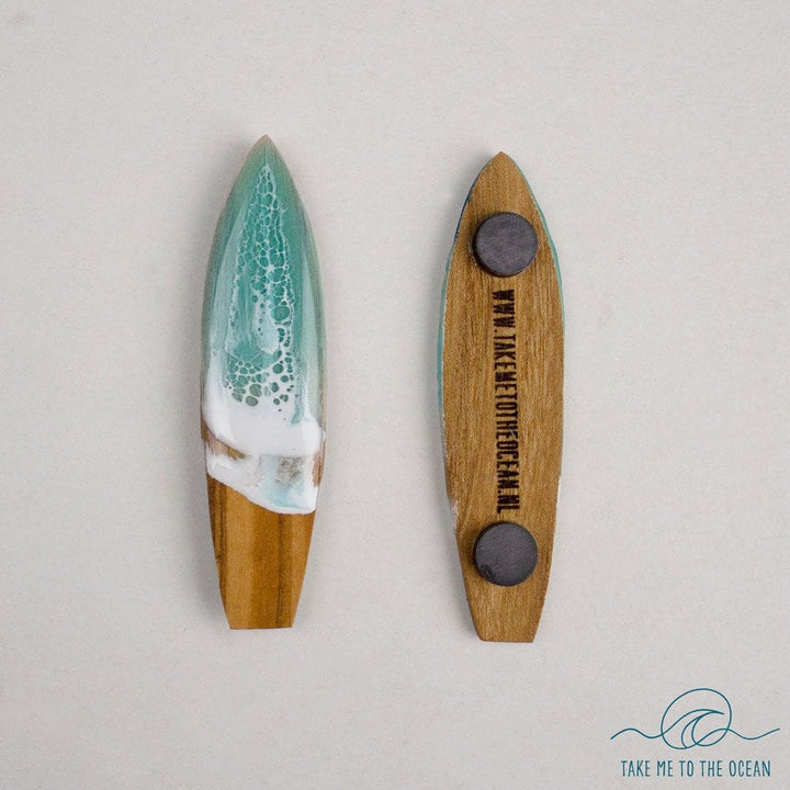 Zwei handgefertigte Surfboard-Magnete von Takemetotheocean aus Holz und Harz sind abgebildet: Einer zeigt grün-weiße nachhaltige Ocean Art, der andere die magnetische Holzrückseite mit Gravur. Logo unten rechts.
