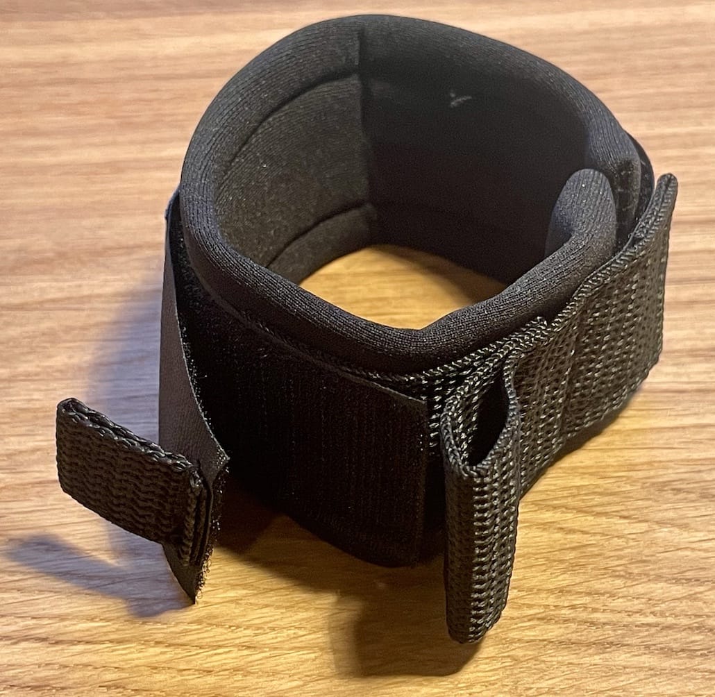 Eine schwarze Klett-Fußfessel (Ersatzteil) von Rapid Surf Shop, mit dicker Polsterung und verstärkten Nähten, wird auf Holz gerollt gezeigt. Das Klettband hat ein offenes Ende zur Befestigung.