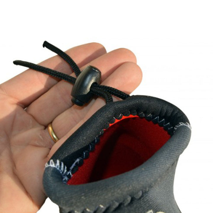 Eine Hand hält einen schwarzen Kordelzug mit Kunststoffstopper, der an der Öffnung des ATAN Madi Neopren Latex Halbschuhs 3mm von Atan befestigt ist. Der Halbschuh wurde für das Windsurfen entwickelt und verfügt über eine innovative Barfusstechnologie.