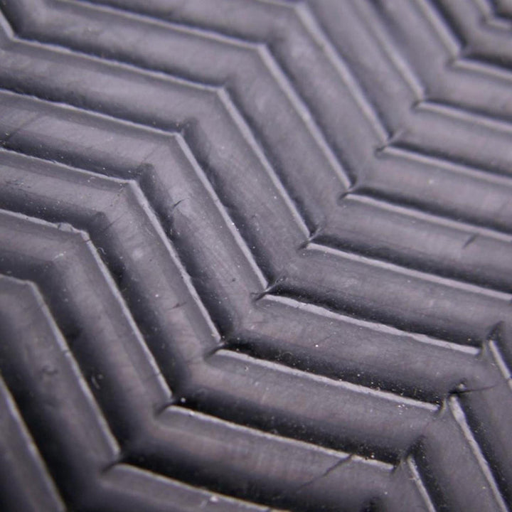 Nahaufnahme einer schwarzen Oberfläche mit einem erhabenen Chevron-Muster, wie der Griff des Atan ATAN Madisson Neopren Latex Schuh 3mm. Sein strukturiertes Gummi hebt die präzise Barfusstechnologie durch geometrische Linien und Rillen hervor.