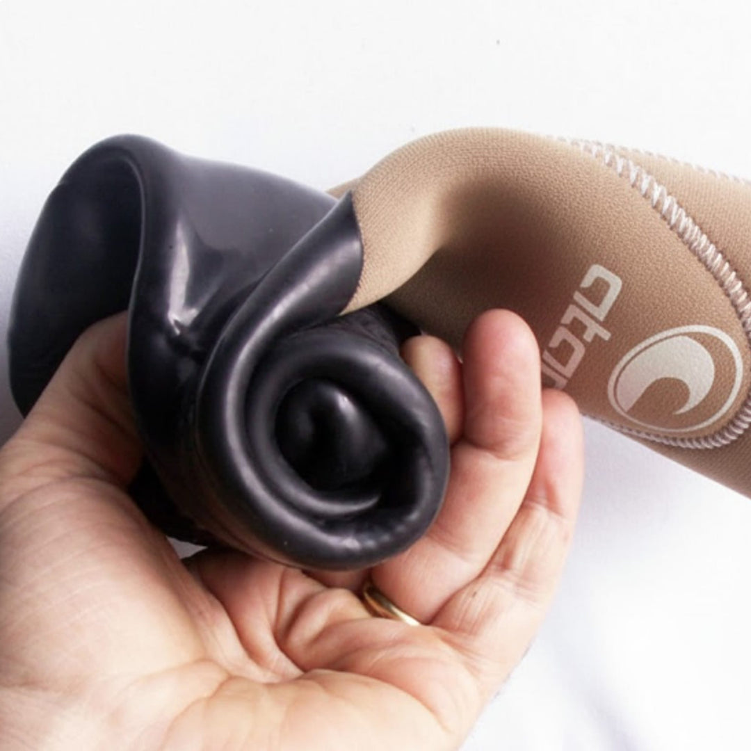 Eine Hand drückt auf den Rand eines ATAN Sunfast Neopren Latex Schuhs 3mm und enthüllt das flexible schwarze Innenfutter von Atan mit Barfusstechnologie für ein barfußähnliches Gefühl und eine hellbraune Außenseite mit weißen Nähten und einem partiellen Logo.