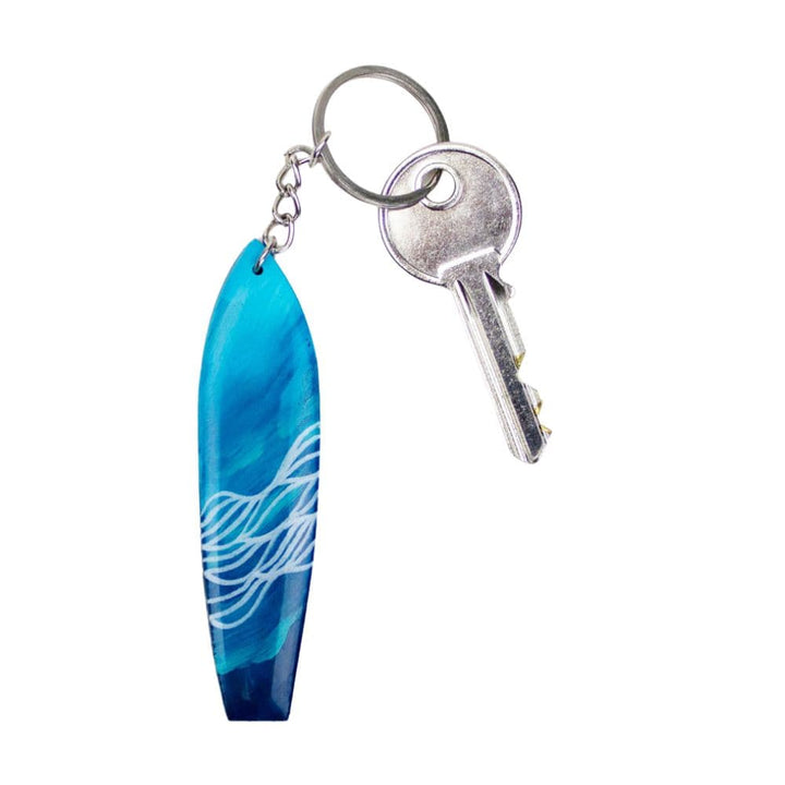 Der Takemetotheocean Surfboard Schlüsselanhänger handgefertigt ist ein silberner Schlüssel an einem Schlüsselring, handgefertigt in blau und weiß mit wellenartigen Resin Ocean Art Mustern.