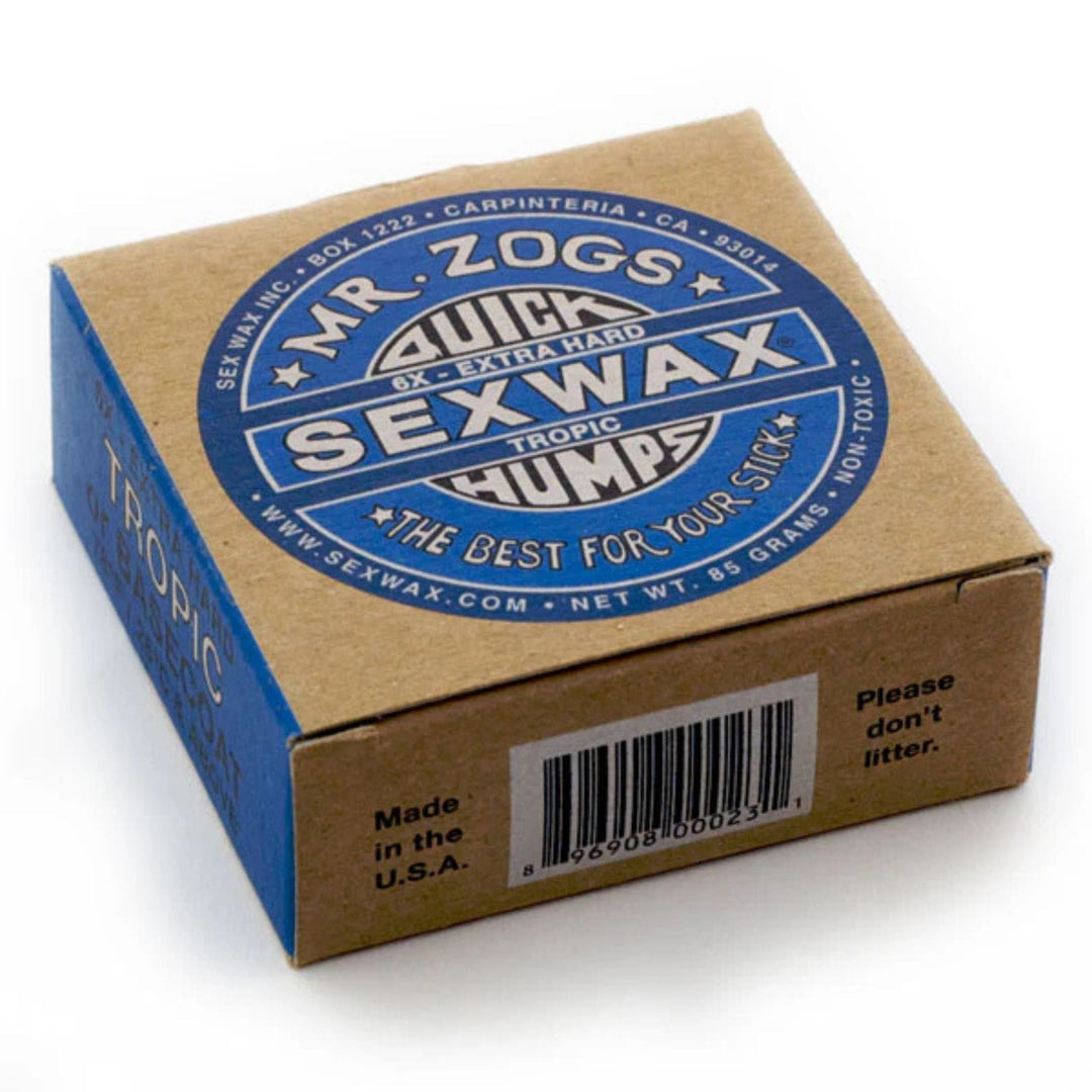 Eine braune Schachtel SEX WAX - Quick Humps Surfwachs von SEX WAX mit einem blauen Etikett mit der Aufschrift "QUICK HUMPS SEX WAX Extra Hard Tropic", Kokosnuss Duft, Produktinfo, Barcode und "Please don&