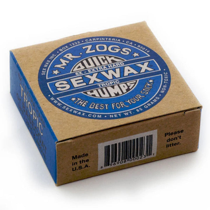 Eine braune Schachtel SEX WAX - Quick Humps Surfwachs von SEX WAX mit einem blauen Etikett mit der Aufschrift "QUICK HUMPS SEX WAX Extra Hard Tropic", Kokosnuss Duft, Produktinfo, Barcode und "Please don&
