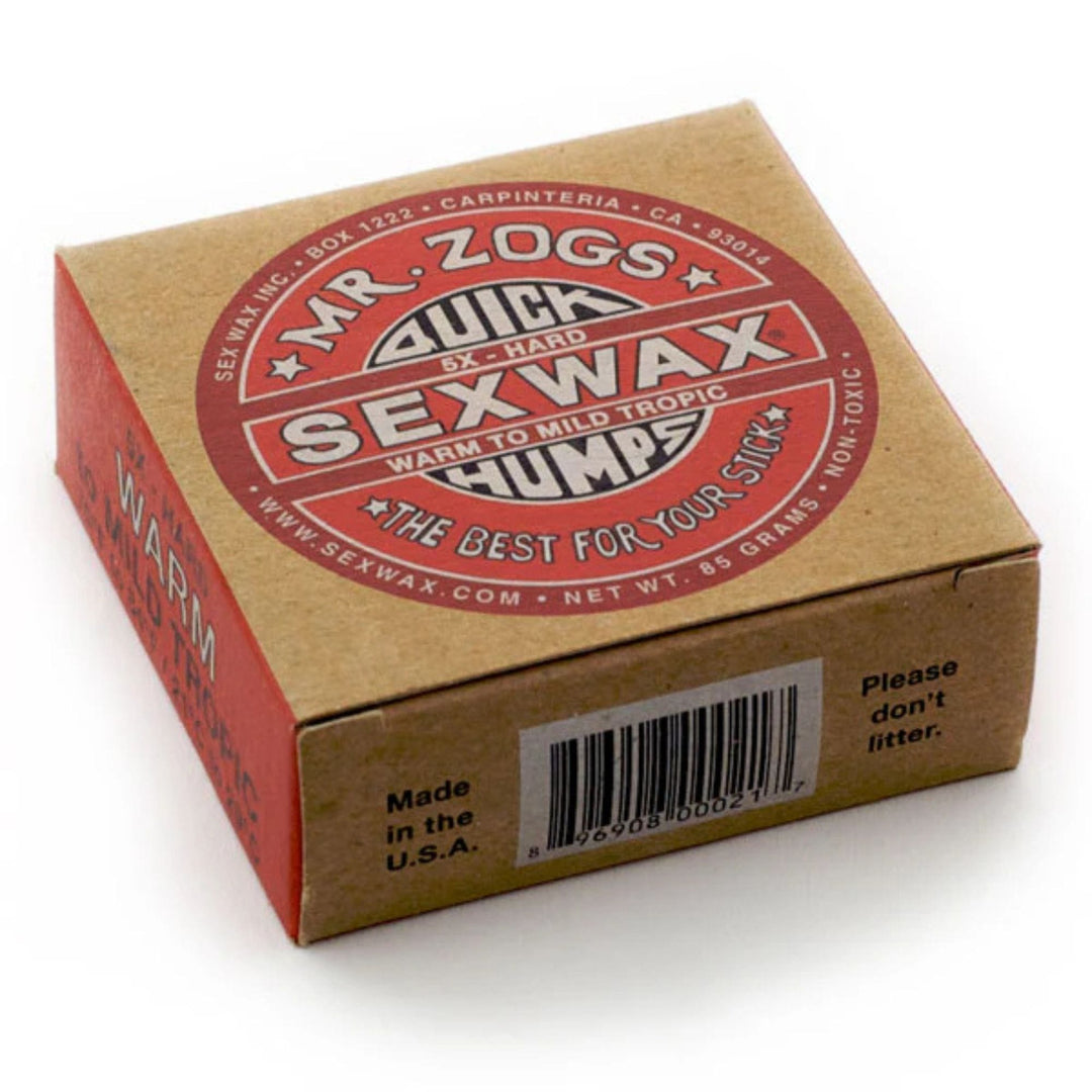 Eine braune Schachtel mit SEX WAX - Quick Humps Surfwachs (extra hart, tropisch warm bis mild), mit einem rot-weißen runden Logo, Barcode auf einer Seite und Kokosnuss Duft. Marke: SEX WAX.