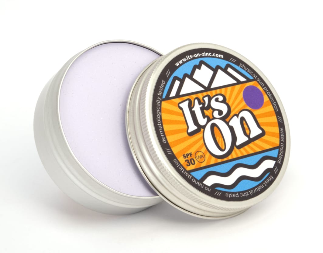 In einer runden Metalldose mit teilweise geöffnetem Deckel befindet sich eine hellviolette Creme. Auf dem bunten Etikett steht It&