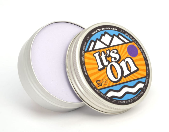 In einer runden Metalldose mit teilweise geöffnetem Deckel befindet sich eine hellviolette Creme. Auf dem bunten Etikett steht It&