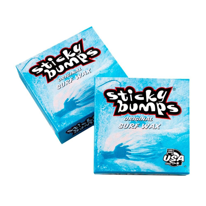 Abgebildet sind zwei blaue Schachteln Sticky Bumps - Surfwachs von Sticky Bumps, jede mit einem Wellenmuster und schwarzem, weißem und rotem Branding. Auf der Verpackung steht "Made in USA" und es wird auf die biologisch abbaubare Formel hingewiesen.