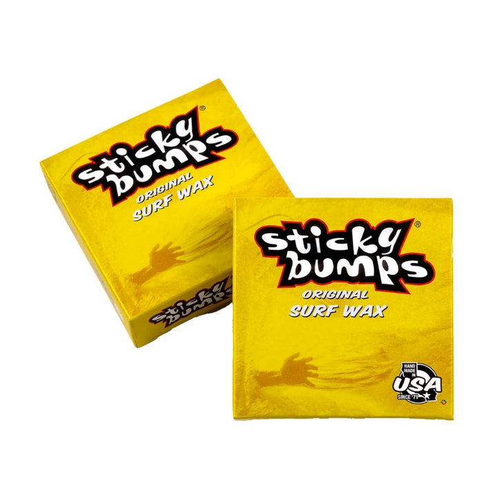 Zwei gelbe Schachteln Sticky Bumps - Surfwachs von Sticky Bumps sind abgebildet - eine flach, eine nach links gekippt. Die Verpackung hat einen fetten schwarzen und weißen Text, ein "Made in USA"-Label und verspricht hervorragenden Surf Grip für dein Board.