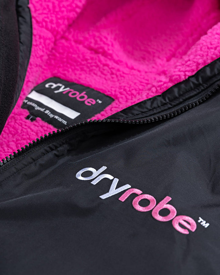 Nahaufnahme der Dryrobe Long Sleeve Schwarz Rosa von Dryrobe - eine schwarze Jacke mit weißem und rosafarbenem Branding, einem weichen rosafarbenen Fleecefutter und einem Innenetikett mit dem Dryrobe-Logo und "Get changed. Bleib warm.