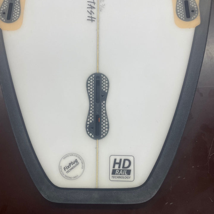 Eine Nahaufnahme des Hecks des Delight Alliance - Stash Riversurfboards zeigt einen mittleren Finnenschlitz, zwei äußere Finnenplugs, eine schwarze Schiene und Aufkleber mit der Aufschrift "HD Rail Technology" und "Futures - Fin Plug Technology".