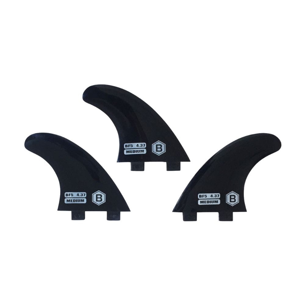 Abgebildet sind drei schwarze Buster-Surfboards Thruster Softfinnen Medium FCS1, jeweils mit weißem B-Logo und doppeltem Tab-Boden für Sicherheit beim Surfen. Die flexiblen Flossen sind nebeneinander angeordnet.