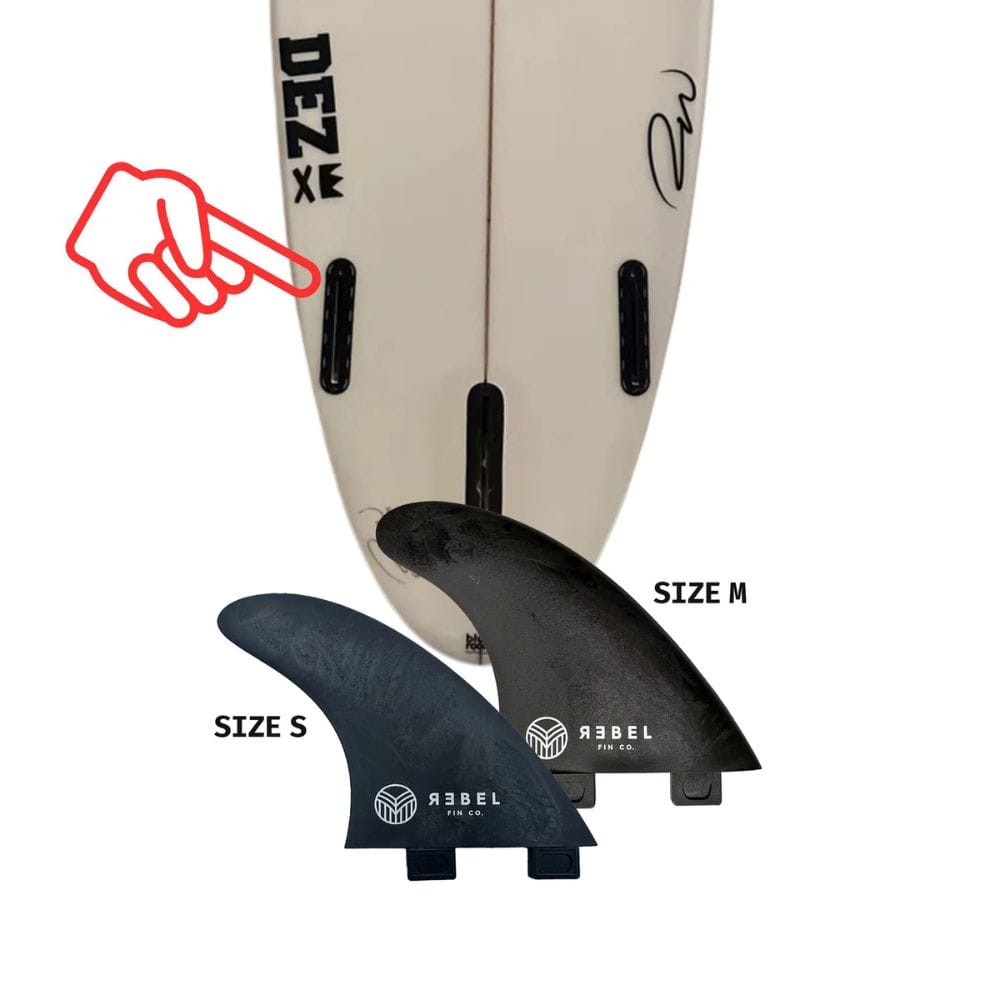 Ein Surfbrett mit zwei schwarzen Finnenkästen steht aufrecht. Davor befinden sich zwei abnehmbare Rebel Fin - einzelne Finne (Carbon) von Rebel Fin, beschriftet mit Größe S und Größe M. Ein rotes Handsymbol zeigt auf einen der Finnenkästen des Surfboards.
