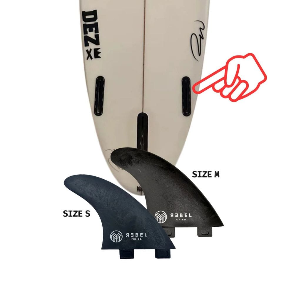 Nahaufnahme eines Surfboard-Heckes mit zwei leeren Finnenschlitzen, einer roten Hand, die auf einen davon zeigt, und zwei Rebel Fin - einzelne Finne (Carbon) von Rebel Fin - mit den Bezeichnungen SIZE S und SIZE M - im Vordergrund.