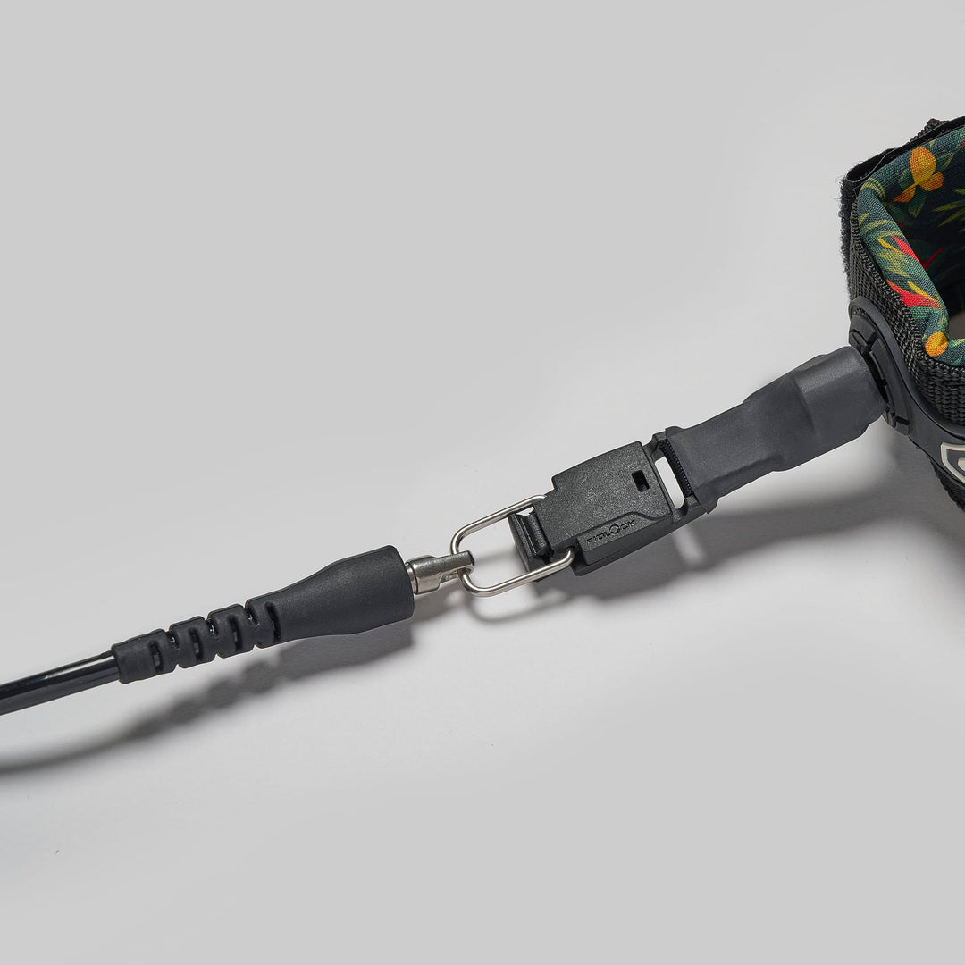 Eine Nahaufnahme der Edgeboards Surfboard Leash mit Quickrelease (Releash) zeigt das floral gemusterte Band, den Metallclip und die schwarze Kunststoffschnalle mit Schnellverschluss, die an die Leash-Systeme von Rapid Surfing erinnern, auf einem schlichten grauen Hintergrund.