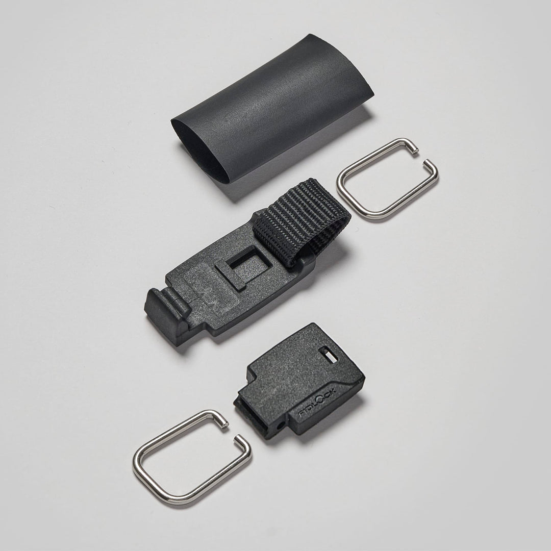 Ein Set aus schwarzen Kunststoff- und Metallteilen - darunter zwei Clips, eine Magnetleash mit ReLeash Verschluss von Rapid Surf Shop, eine kleine Abdeckung und ein rechteckiges Stück - sind auf grauem Grund angeordnet, ideal für Rapid Surfing Essentials.