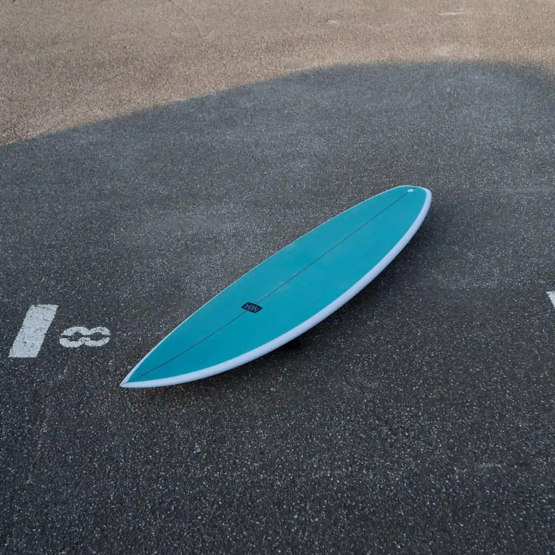 Ein türkisfarbenes NOA Surfboards - Pocket Knife 2.0 von NOA mit weißem Rand liegt kopfüber auf dem Asphalt, teilweise innerhalb eines markierten Parkplatzes mit der Nummer 18.