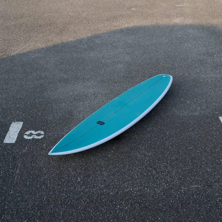 Ein türkisfarbenes NOA Surfboards - Pocket Knife 2.0 von NOA mit weißem Rand liegt kopfüber auf dem Asphalt, teilweise innerhalb eines markierten Parkplatzes mit der Nummer 18.