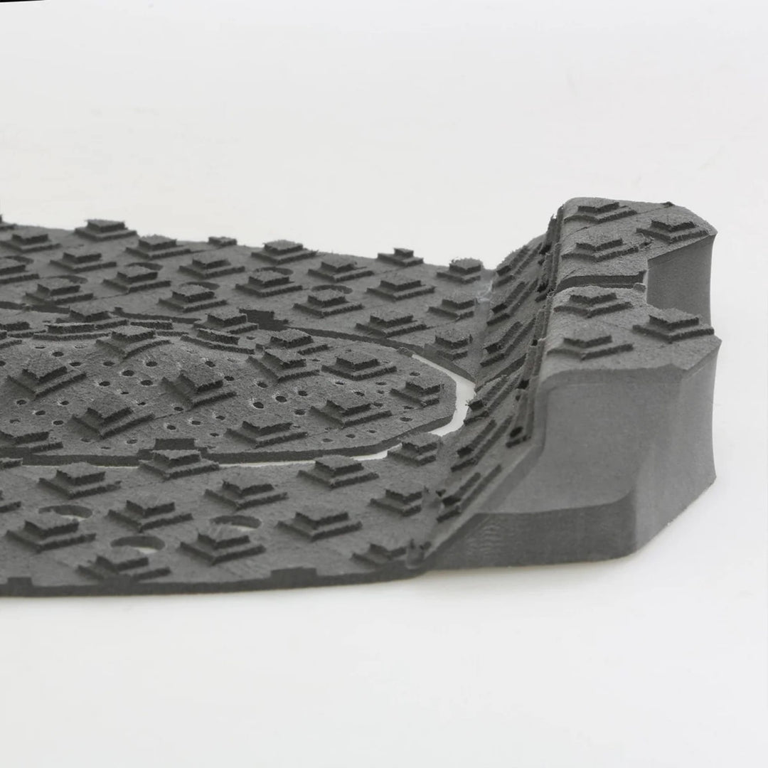 Eine Nahaufnahme einer grauen Gummifußmatte mit erhabenen, kantigen Profilen und einer erhöhten Kante, ähnlich dem strukturierten Griff des FCS T-3 Eco Eclipse Tailpad von FCS.